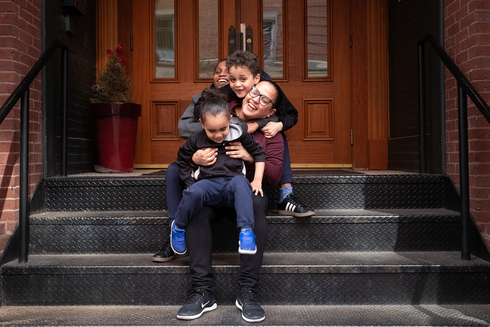 A mother and her three children in the USES Family Mobility program is sitting on porch steps and hugging one another.